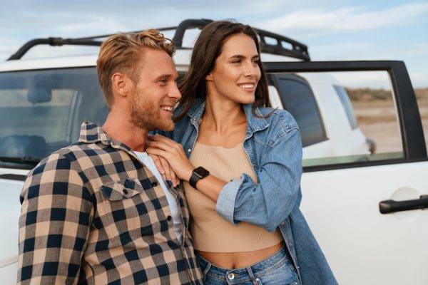 Beautiful young smiling couple while bonding to each other and leaning at their car